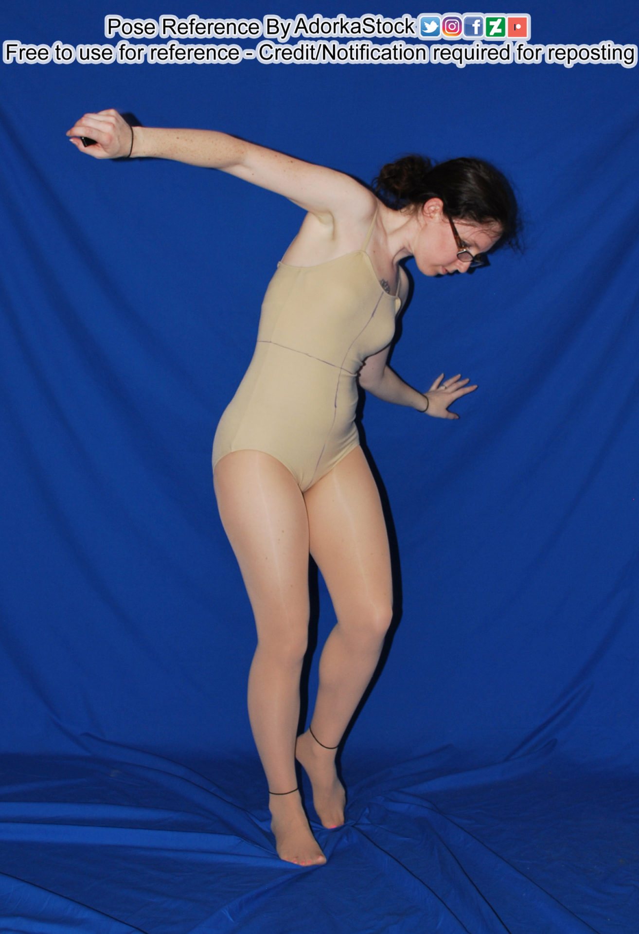 A woman in a tan bodysuit jumping into the air, looking down and appearing to float with her right arm raised behind her and the left stretched out to the side