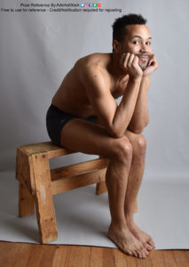 A Latino man sitting on a wooden bench, angled to the right, with his elbows on his knees. He's smiling a little and looking at the camera