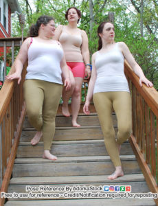 A low angle picture of three women walking down a set of stairs. The one at the top is wearing a nude colored body shaper top, pink shorts and looking to the left. The second one down is wearing a white shirt and olive green leggings, is looking to the right, smiling and has her hand just above the banister. The third one down is wearing the same outfit, looking to the right wistfully and has her arm resting on the banister
