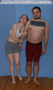 Thin, white, female pose reference model grabbing the arm of a stocky, white, male pose reference model as if to drag him off but he looks unsure.