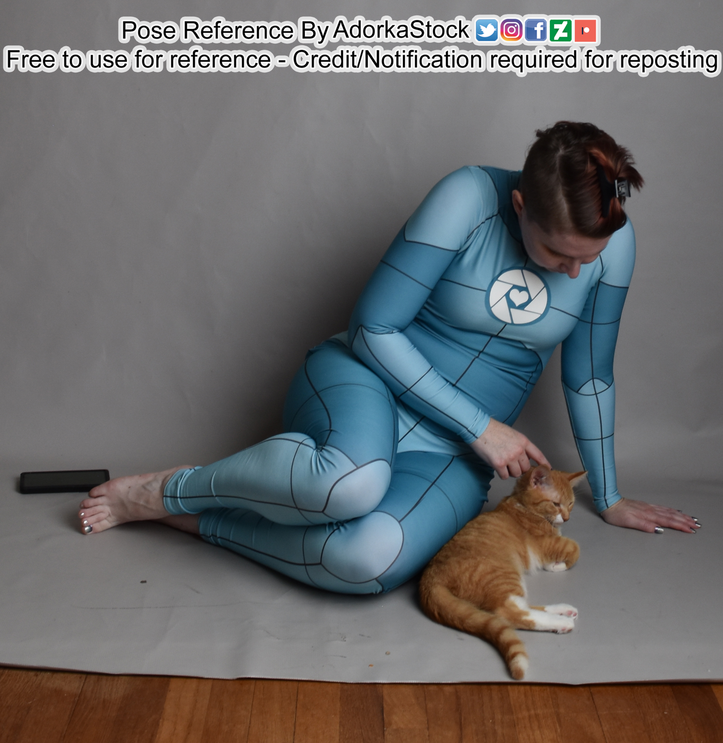 Thin, white, female pose reference model in sitting pose with grid suit. Beside her is a little orange kitten and she's looking down and petting it.