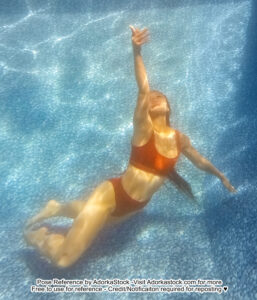 A woman wearing a red bikini floating at the bottom of a pool, reaching upwards.