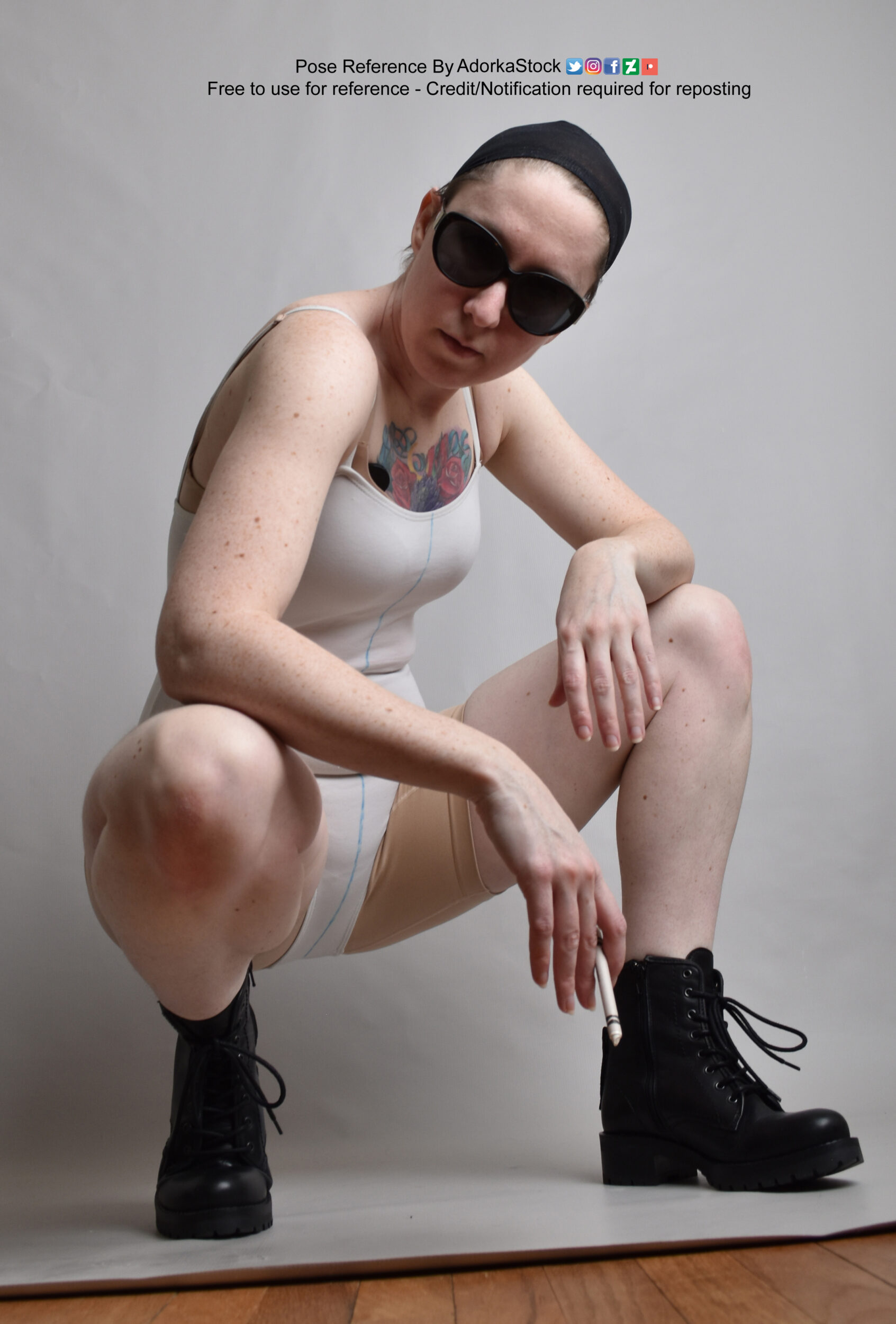Thin, white, female pose reference model in crouching pose with a crayon held like a cigarette, sunglasses, and big black boots. It's from a low angle.