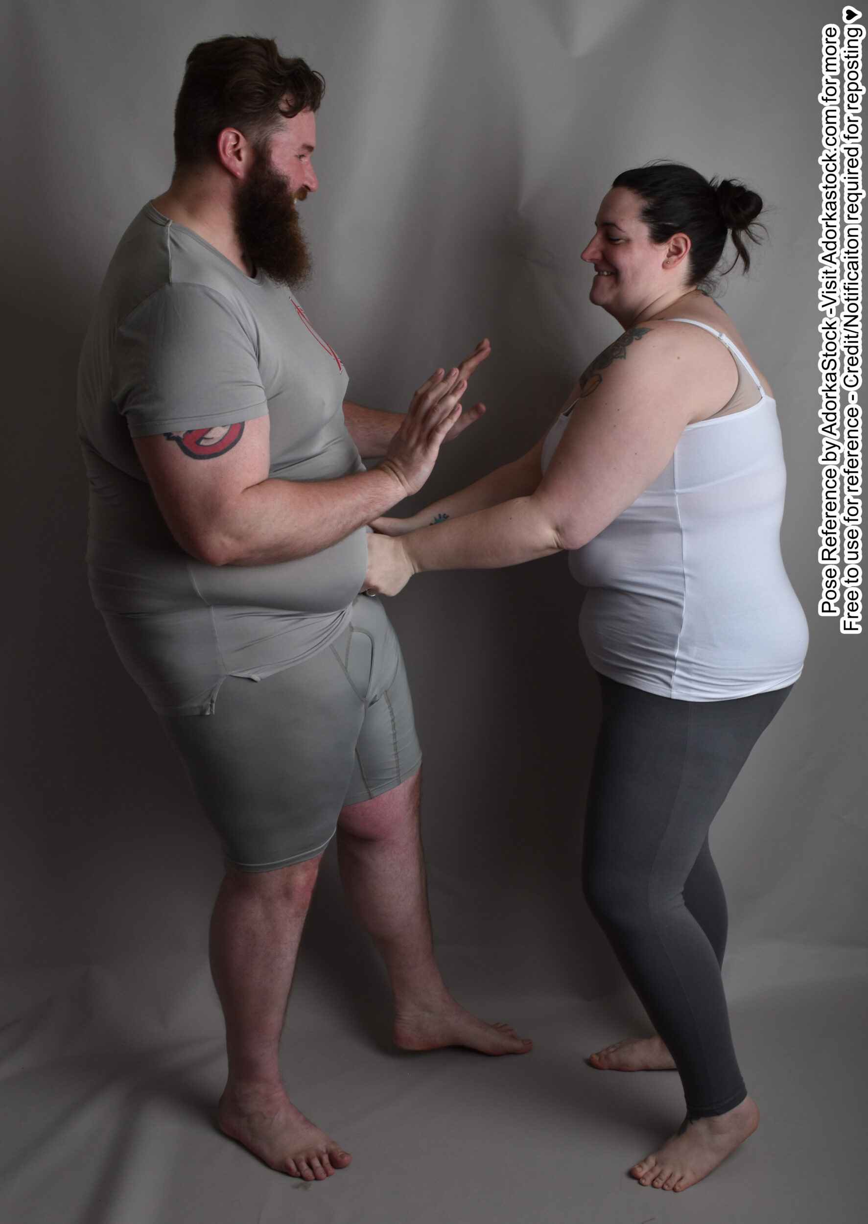 Fat, white, female pose reference model in standing pose with a fat, white male model, attacking him with tickles in the belly while he raises his arms in pleading.
