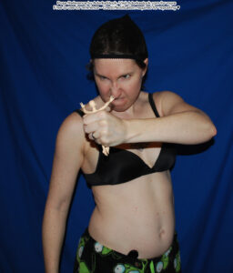 Thin, white, female pose reference model in waist up pose with a small ball jointed figure grasped in her fist. She's looking at it with malice and the figure is posed as if flailing.