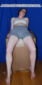 Thin, white, female pose reference model in sitting pose with foreshortening, legs handing in front.