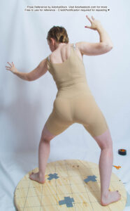 White woman wearing a skin colored leotard, photo taken from behind, hands in the air like she is casting a spell.