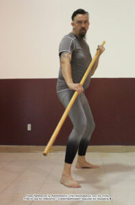 Tall, fit, male pose reference model in standing pose with staff in two hands and a serious expression.