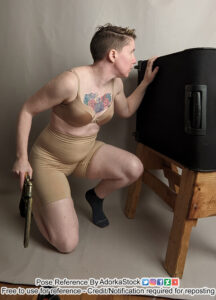Thin, white, female pose reference model in kneeling pose with one knee up, hiding behind cover, with a handgun down by her side.