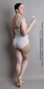 Thin, white, female pose reference model in back pose with a wine glass, glancing over her shoulder, with one foot lifted slightly.