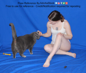 A white woman sitting cross-legged while petting a grey cat.