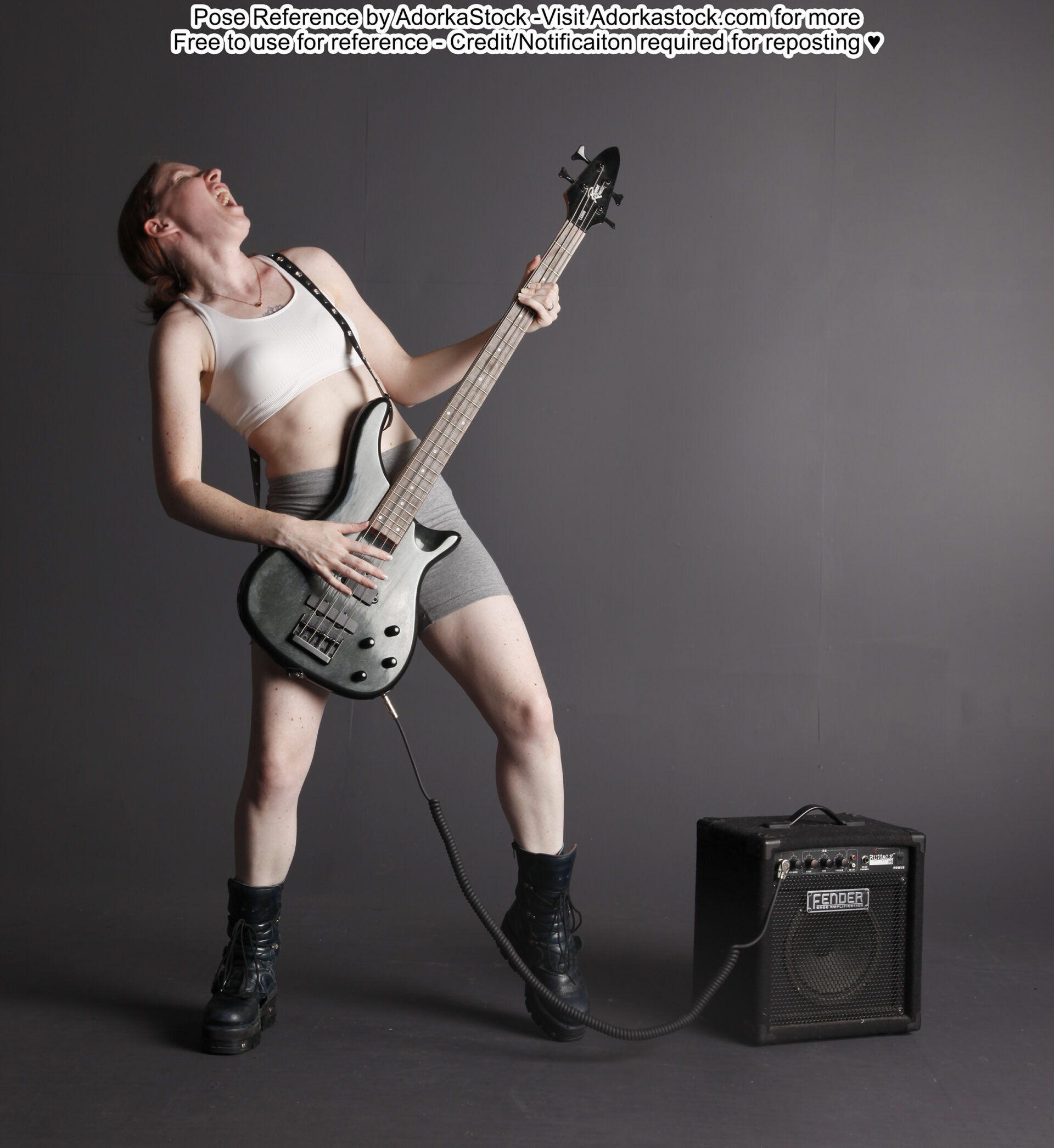Thin, white, female pose reference model in standing pose with a base guitar and amp, rocking out with her head back.