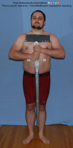 Socky male pose reference model in stiff standing pose with a sword held blade down with the hilt at chest height