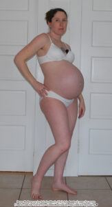 Pregnant to term, white, female pose reference model in standing pose with one hand on a hip