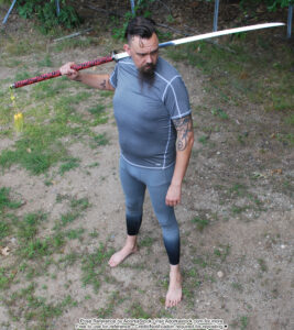 tall, fit, male pose reference model in high perspective, standing pose with a sword over his far shoulder, he is looking back