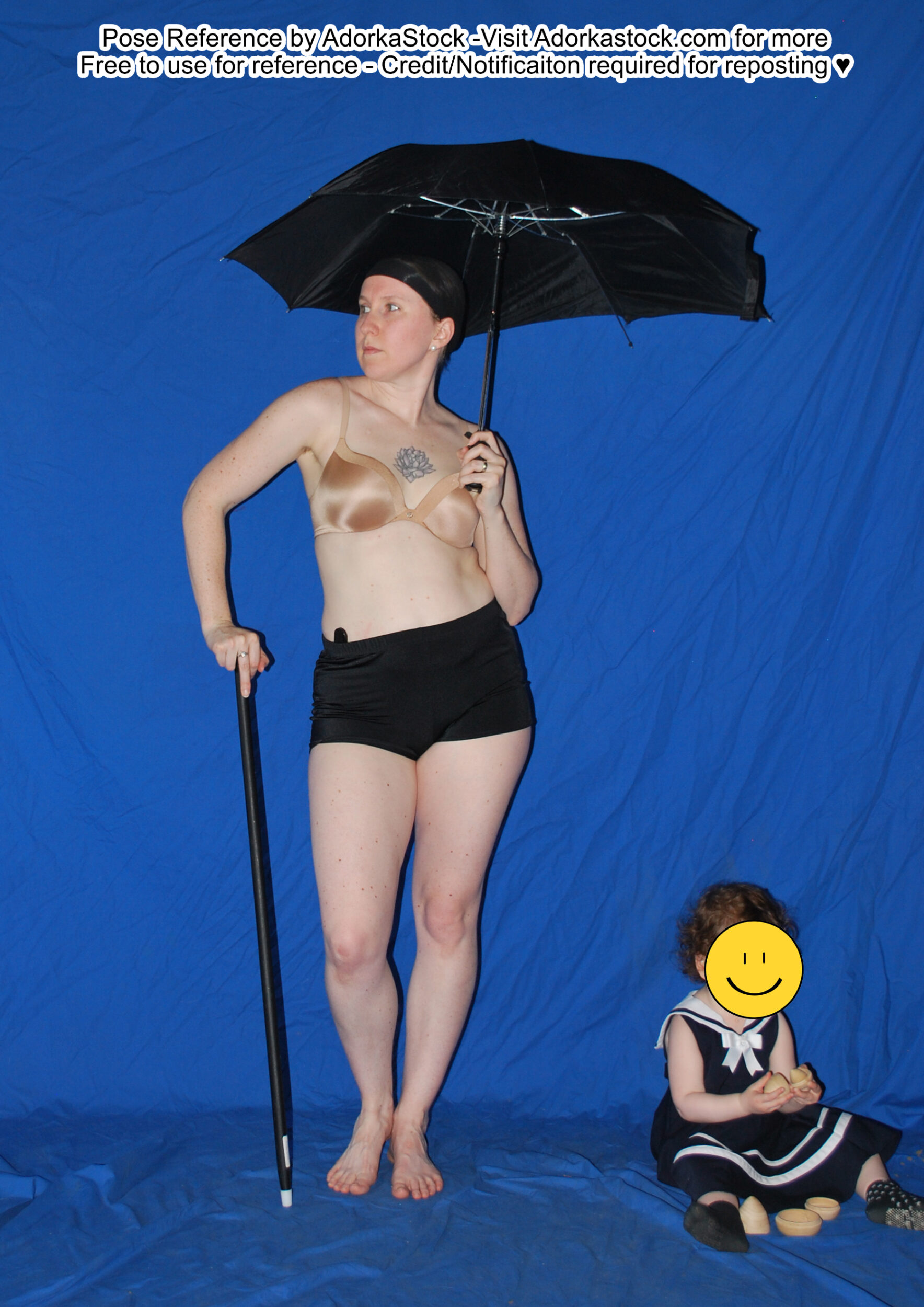 Thin white female model standing with a cane in one hand which she leans on while the other hand holds up a somewhat tattered looking umbrella. She's looking off to the left and on the ground beside her a toddler sits holding a toy egg that comes apart into two pieces.