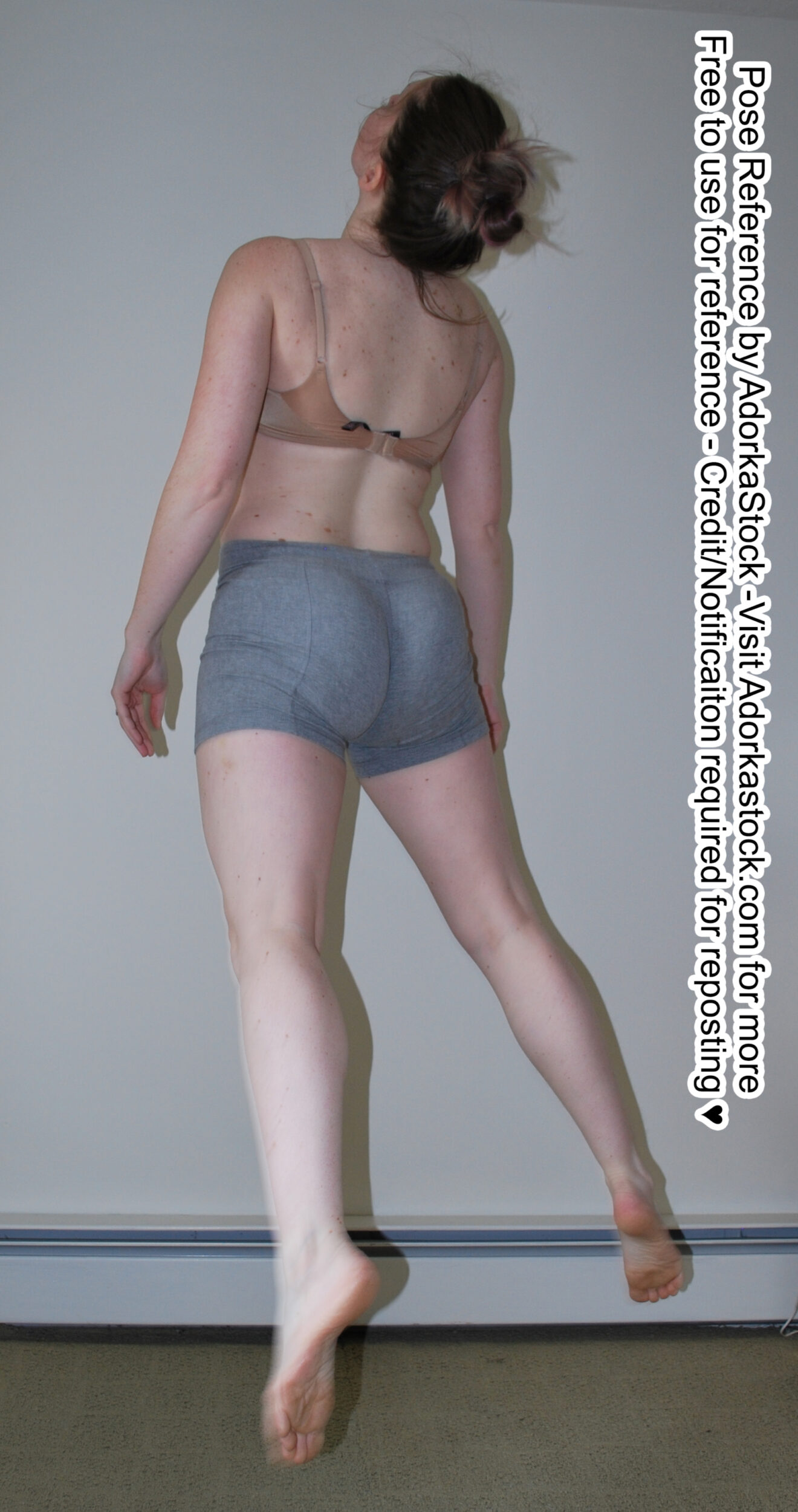 Thin female model with her back to the viewer floats just off the ground. She is looking up, with her arms at her side and her legs apart, toes pointed.