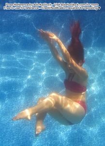Fit, Asian female model underwater and floating with legs out and arms up, hair flowing above her head