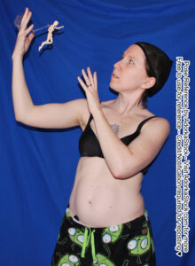 waist up image of a thin white female model with arms raised, palms open towards a tiny figure floating in the air beside her