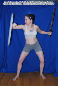 thin white female pose reference model holding a short sword and makeshift shield in a side defense posture