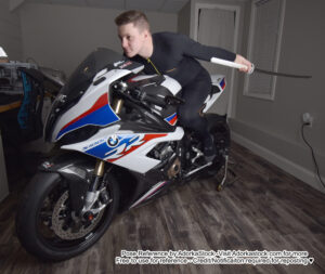 Fit, white, male model riding a motorcycle with a katana in one hand held behind him