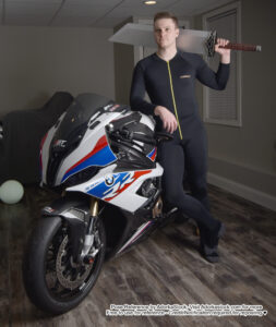 white fit male model standing casually next to a motorcycle holding a large prop sword