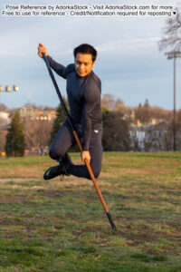 fit Asian male model throwing himself forward with a staff in the ground