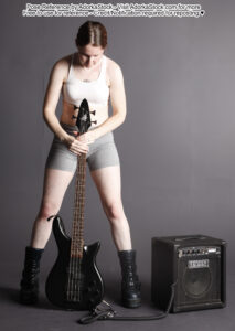 Thin white female model holding a bass guitar in front of herself and looking down at it
