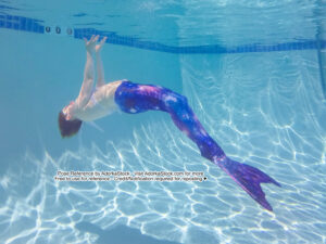 thin white female model wearing a mermaid tail underwater reaching up to the surface