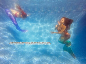 two thin Asian female models underwater with mermaid tails