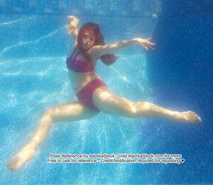Thin Asian female model floating underwater, legs spread wide apart, one arm straight out, the other bent and over her head, looking as if she's caught floating mid-dance.