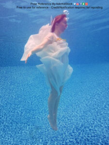 A white woman wearing a frilly white dress, sinking in water, her arms extended, legs pointed and together.
