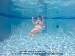A white woman swimming in a light colored bathing suit completely submerged, looking over her shoulder at the camera.