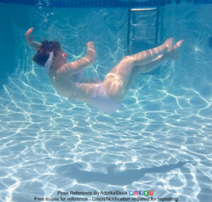 A white woman floating underwater, on her side, back facing the bottom of the image, legs upwards.