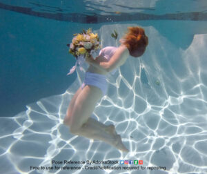 underwater pose of a thin, white, female model with legs back 90° and head tipped back, mostly blocked by floating hair. She is holding a bouquet of flowers.