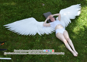 thin white female model lying on the ground looking up with large wings behind her