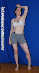 Thin white female model standing with one heel raised and one hand over her head