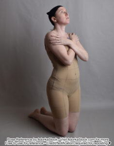 Thin white female model kneeling at 3/4 to the camera, arms crossed over her chest, looking up slightly