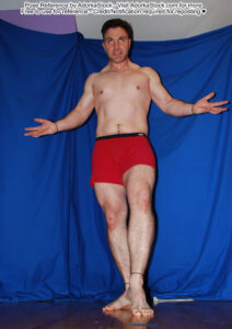 Fit white male model from a low perspective, taking a step, arms and fingers outspread