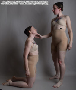 Two thin female models, one kneeling and the other reaching down to touch the kneeling person's chin