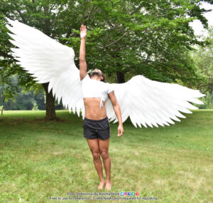 thin Latino model standing with massive wings opened, one arm raised up while he's looking up