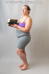 Fat white female model standing in profile, wearing glasses, with a pile of books in her hands