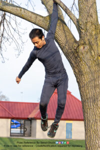 thin asian male model hanging from a tree limb with one arm