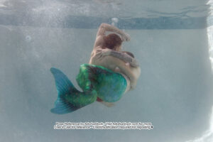 two male models underwater one is wearing a merman tail and the other is not and they are interlocked as if fighting but maybe not...