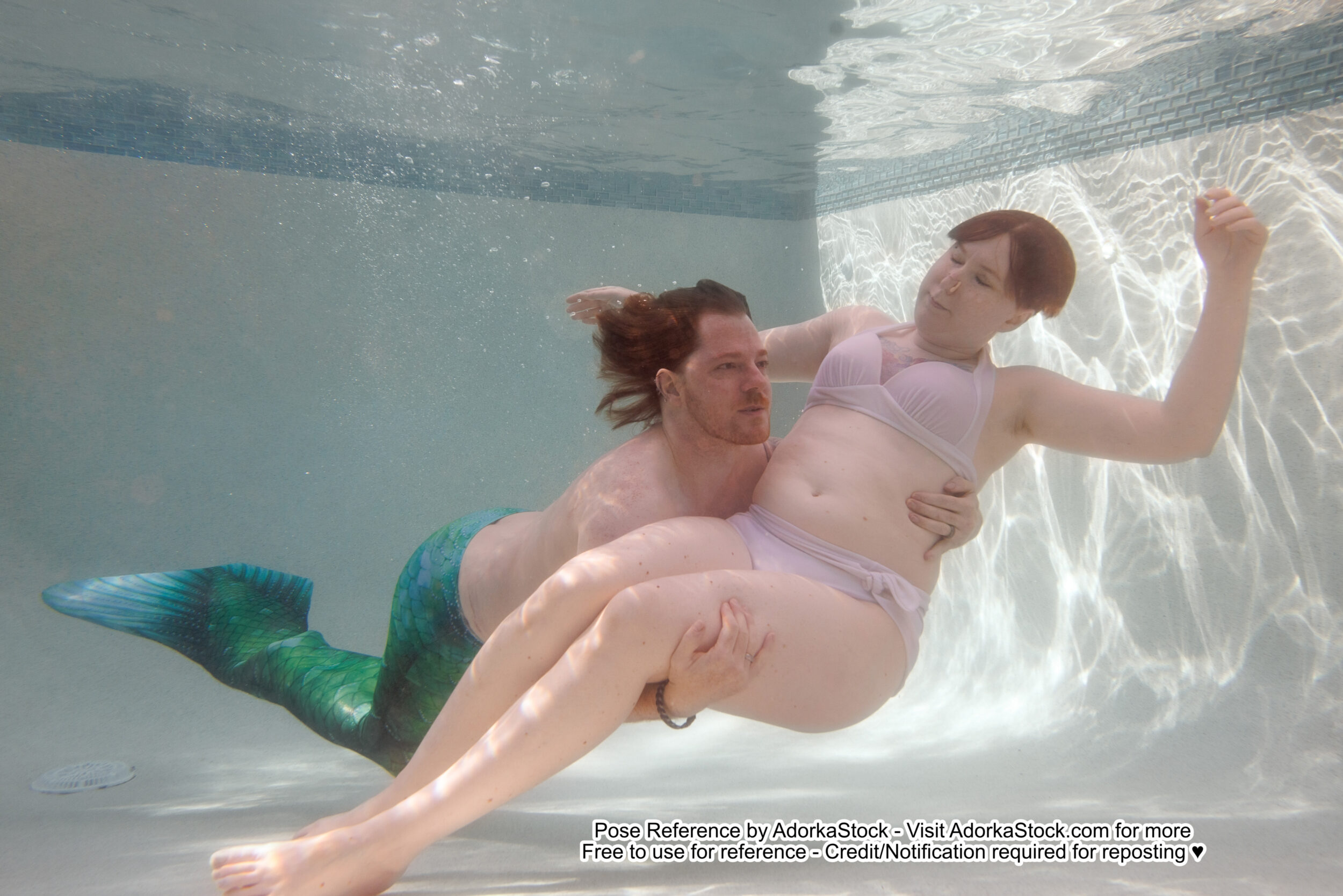 a merman swims through the water and scoops up a floating woman in his arms