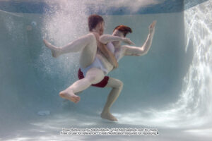 two models underwater the fit male model is holding the female model by the waist and she is flailing