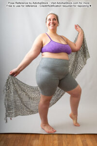fat white female model standing in a pose with weight shifted to one foot, arms out to her side holding a scarf behind her and wearing a sparkly tiara