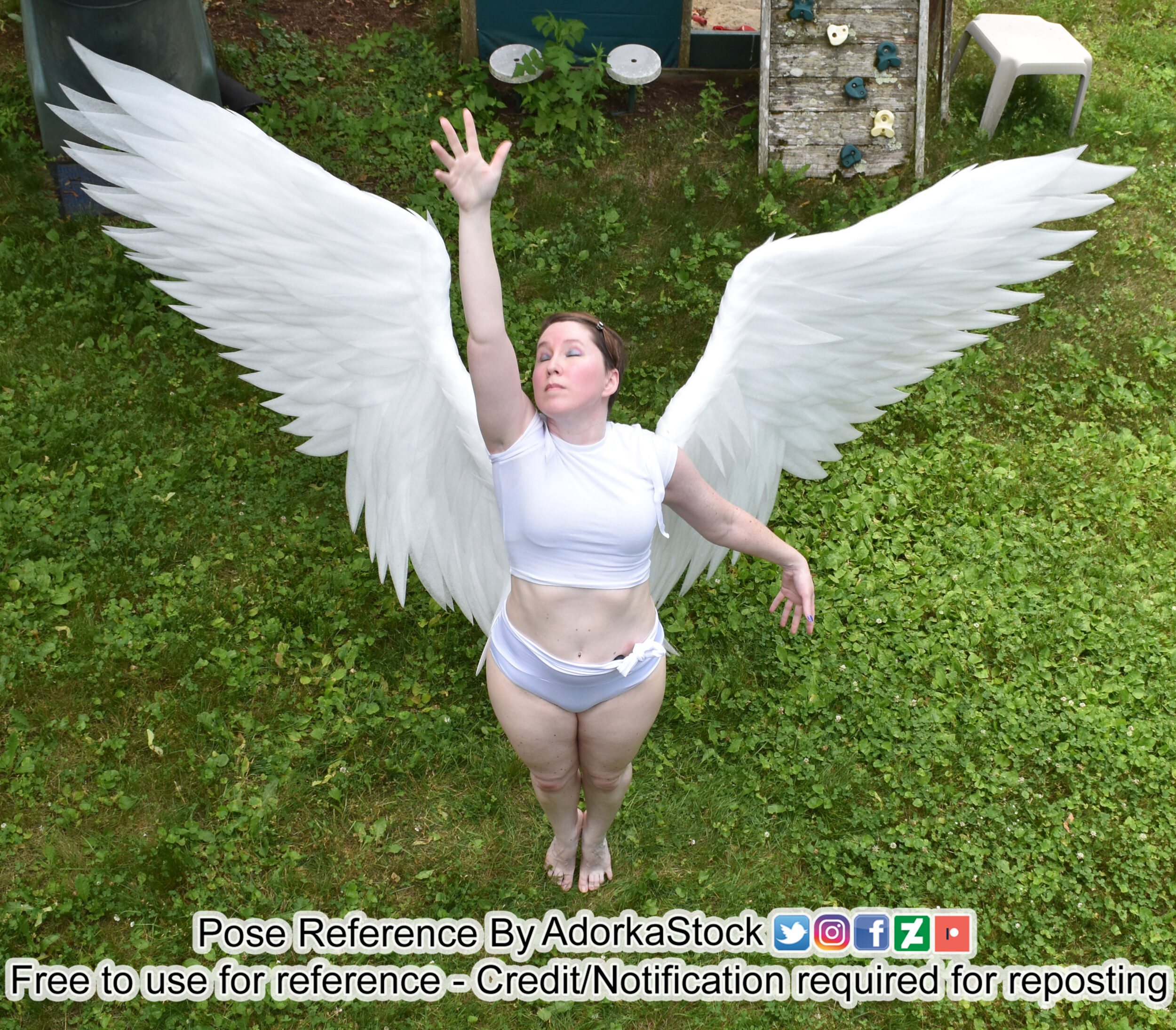 Thin white female model wearing huge wings reaching up with one hand from a high angle
