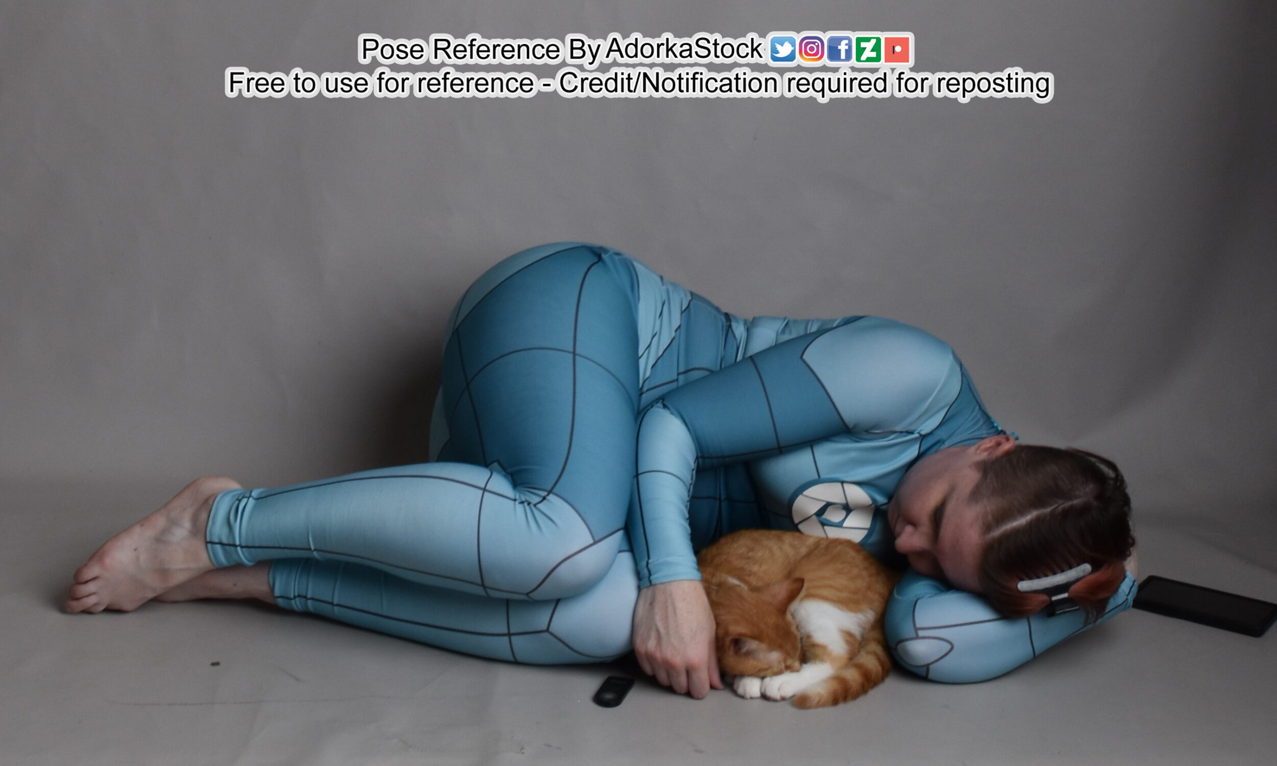 Thin white model in a grid suit curled up on the floor around a small orange and white cat