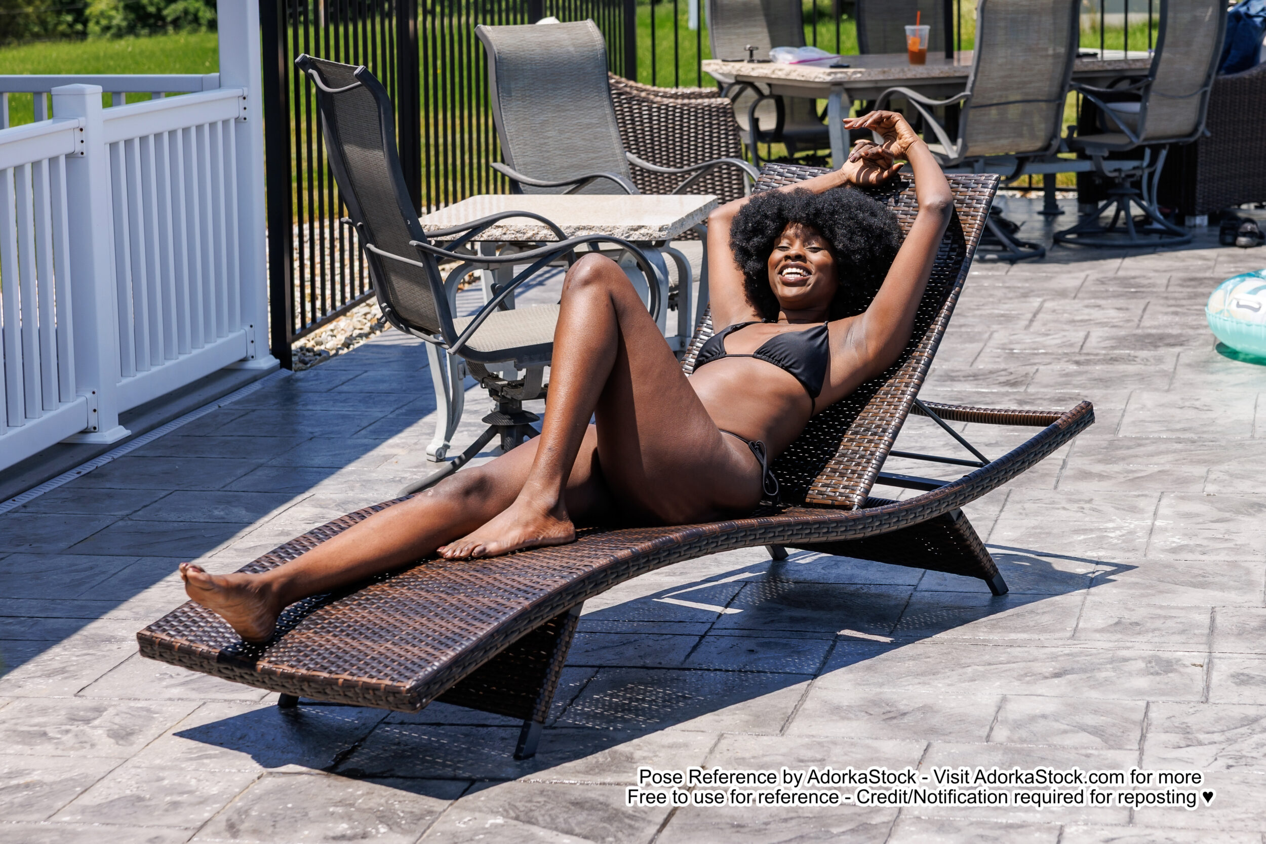 thin Black model reclined on a deck chair with one knee raised and hands over our head